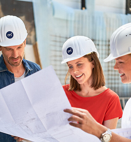 Monvest – Baustellenbesprechung mit Bauplan Team von Monvest Immobilien bespricht Baupläne auf der Baustelle